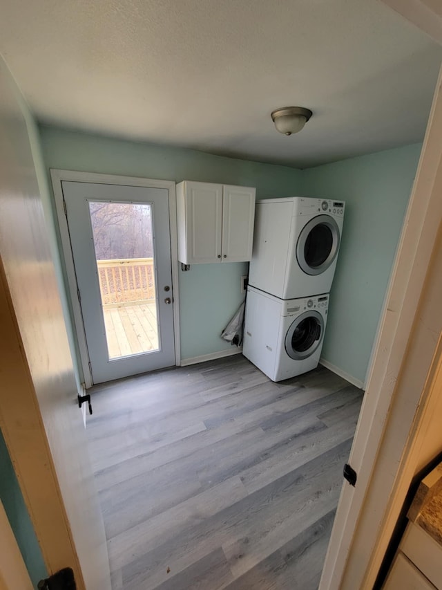 laundry area featuring cabinets, stacked washer / dryer, and light hardwood / wood-style flooring