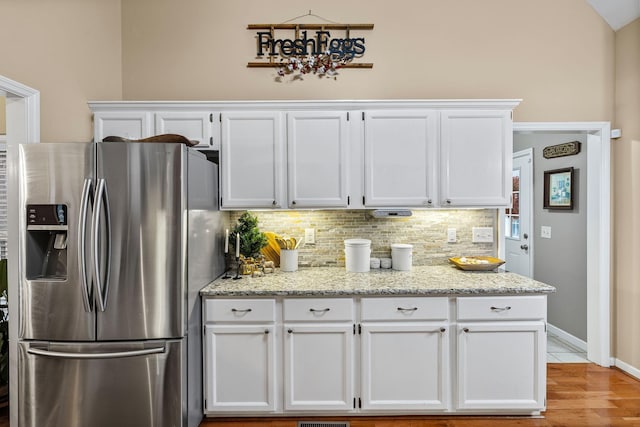 kitchen with light stone counters, stainless steel fridge, light hardwood / wood-style floors, vaulted ceiling, and white cabinets