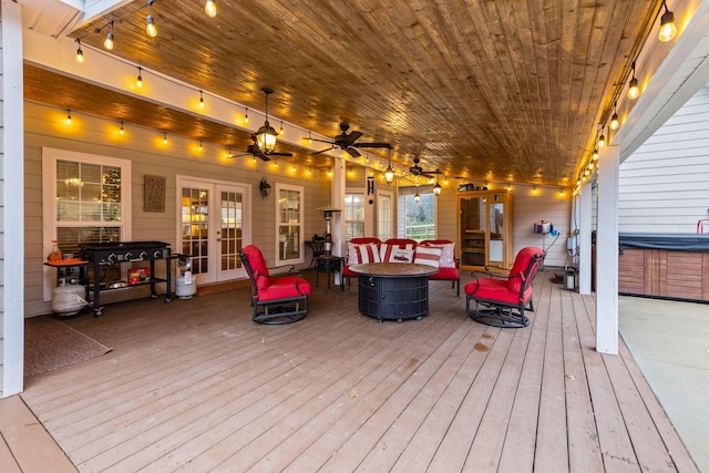 wooden terrace with french doors, a hot tub, ceiling fan, and an outdoor living space with a fire pit