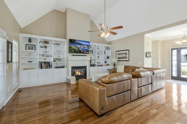 living area with high vaulted ceiling, ceiling fan with notable chandelier, baseboards, light wood-type flooring, and a glass covered fireplace