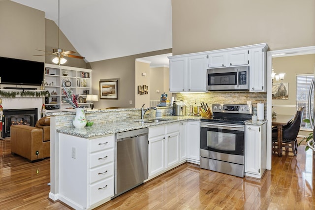 kitchen with a glass covered fireplace, appliances with stainless steel finishes, open floor plan, a peninsula, and a sink