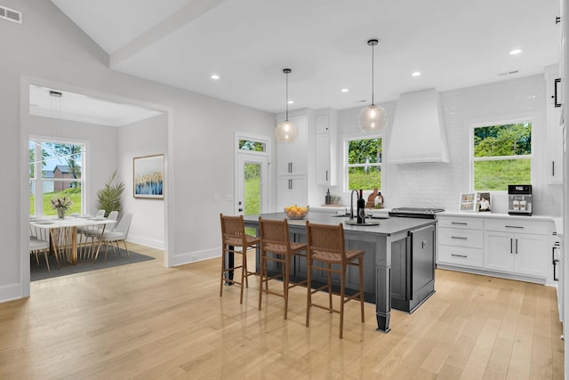 521 Matthew Miller Dr, Smyrna, TN 37167 - kitchen featuring white cabinetry, premium range hood, light wood-style floors, a kitchen island, and a breakfast bar area