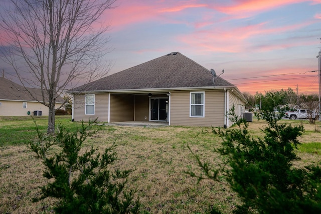 back house at dusk with central air condition unit, a patio, and a yard