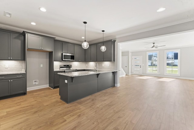 kitchen with light stone countertops, hanging light fixtures, stainless steel appliances, and light hardwood / wood-style floors