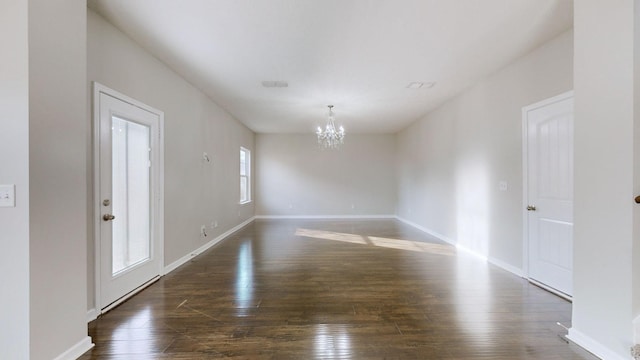 empty room with dark hardwood / wood-style flooring and an inviting chandelier