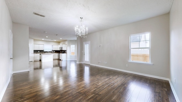 unfurnished living room featuring dark hardwood / wood-style flooring, a chandelier, and a textured ceiling