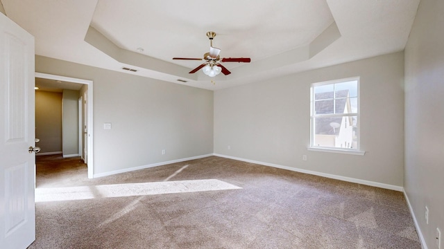 unfurnished room with ceiling fan, a raised ceiling, and light colored carpet