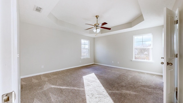 carpeted spare room featuring ceiling fan, a healthy amount of sunlight, and a raised ceiling