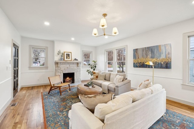 living room with a stone fireplace, a chandelier, and light hardwood / wood-style flooring