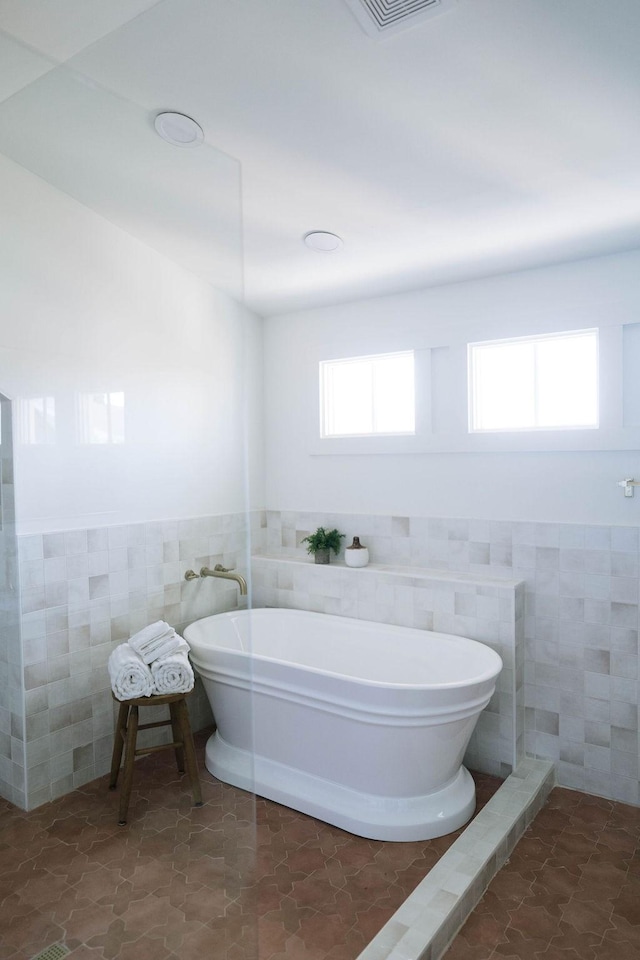 bathroom with a bathing tub, tile patterned flooring, and tile walls