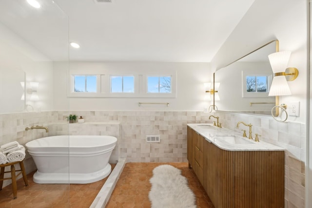 bathroom with tile walls, tile patterned flooring, a bathtub, and vanity