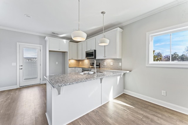 kitchen featuring stainless steel appliances, sink, pendant lighting, light hardwood / wood-style floors, and white cabinetry