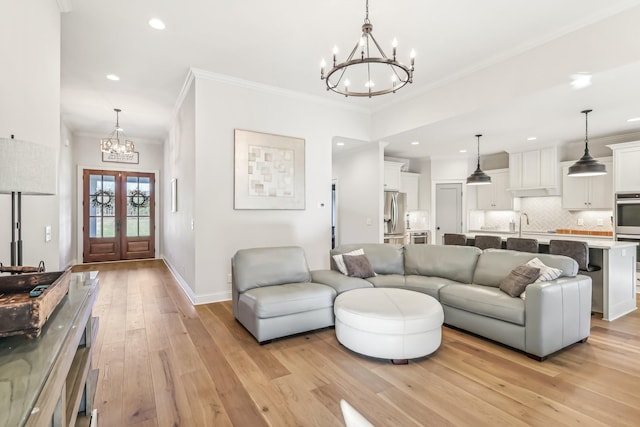 living room featuring french doors, sink, light hardwood / wood-style flooring, a notable chandelier, and ornamental molding