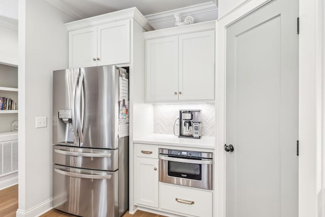 kitchen featuring white cabinetry, stainless steel appliances, tasteful backsplash, light hardwood / wood-style flooring, and crown molding