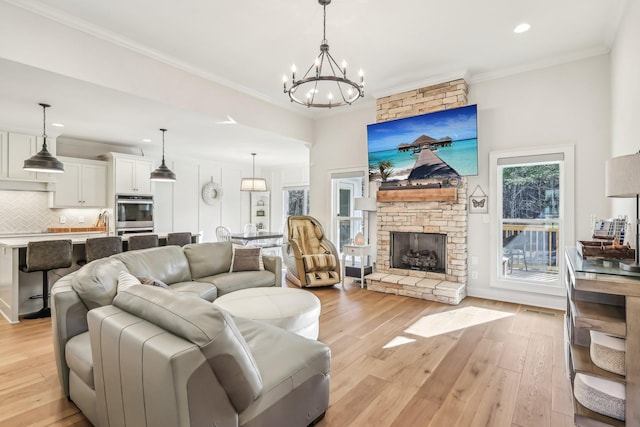 living room with a stone fireplace, light hardwood / wood-style flooring, a chandelier, and ornamental molding