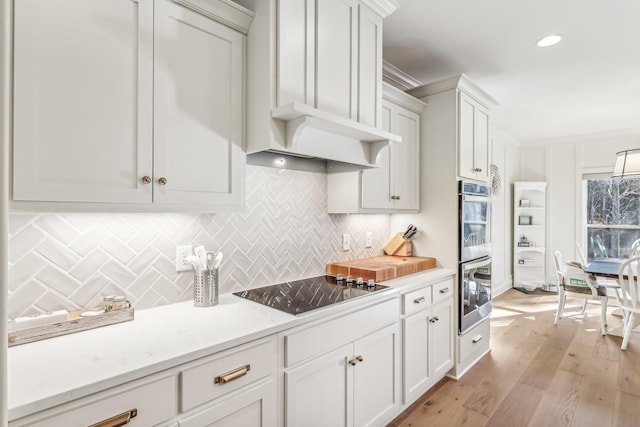 kitchen with black electric stovetop, white cabinets, double oven, tasteful backsplash, and light hardwood / wood-style floors