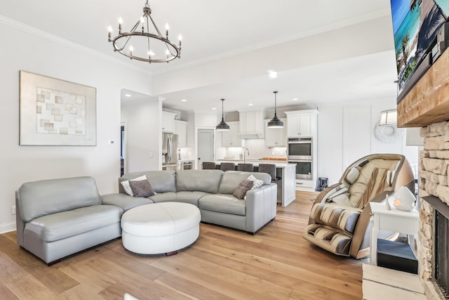 living room with light wood-type flooring, crown molding, sink, a notable chandelier, and a stone fireplace