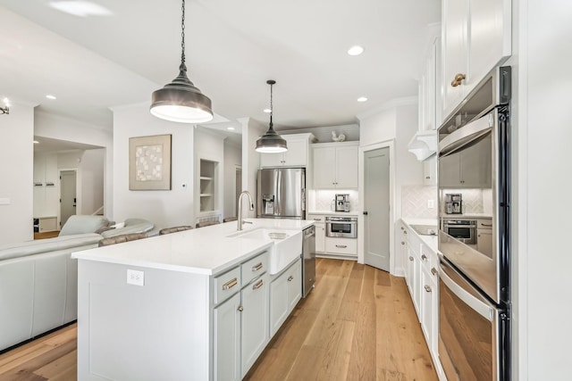 kitchen with appliances with stainless steel finishes, a kitchen island with sink, decorative light fixtures, light hardwood / wood-style flooring, and white cabinetry