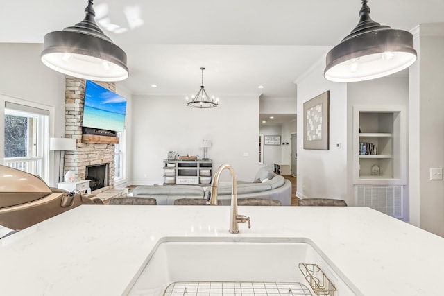 kitchen featuring built in shelves, sink, decorative light fixtures, a chandelier, and a stone fireplace