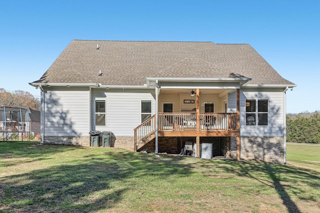 rear view of property with a lawn, ceiling fan, a trampoline, and a wooden deck