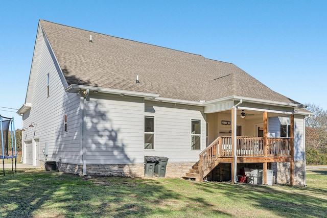 back of house with ceiling fan, a trampoline, and a yard