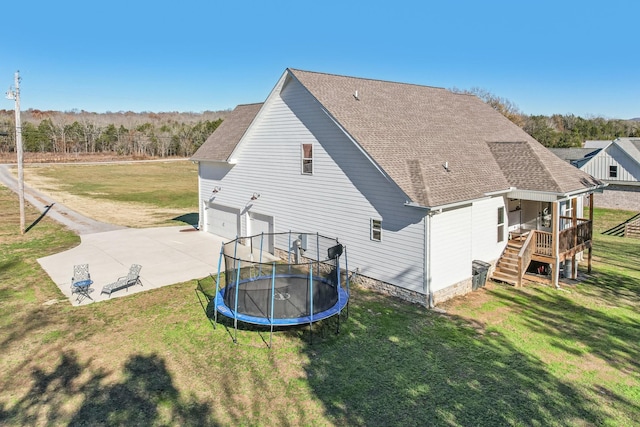 rear view of property with a garage, a trampoline, a yard, and a patio