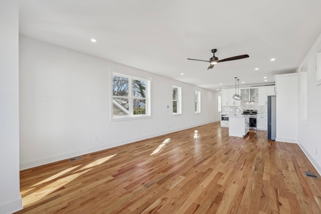 unfurnished living room with ceiling fan, light hardwood / wood-style floors, and sink