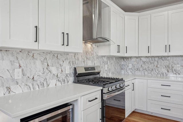 kitchen featuring white cabinets, wall chimney exhaust hood, decorative backsplash, light wood-type flooring, and appliances with stainless steel finishes