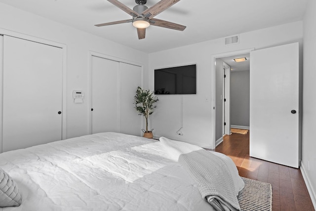 bedroom featuring ceiling fan, dark hardwood / wood-style flooring, and two closets