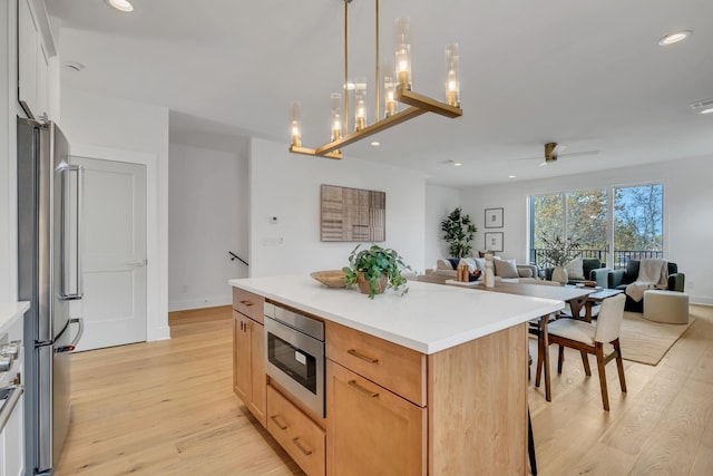 kitchen with stainless steel appliances, light hardwood / wood-style floors, decorative light fixtures, a kitchen island, and ceiling fan with notable chandelier