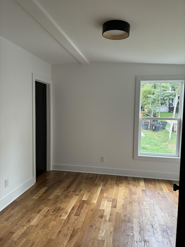 unfurnished room featuring hardwood / wood-style flooring and beamed ceiling