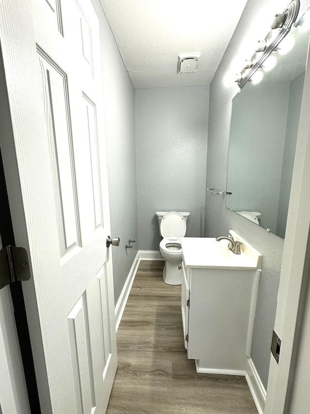 bathroom with wood-type flooring, toilet, vanity, and a textured ceiling