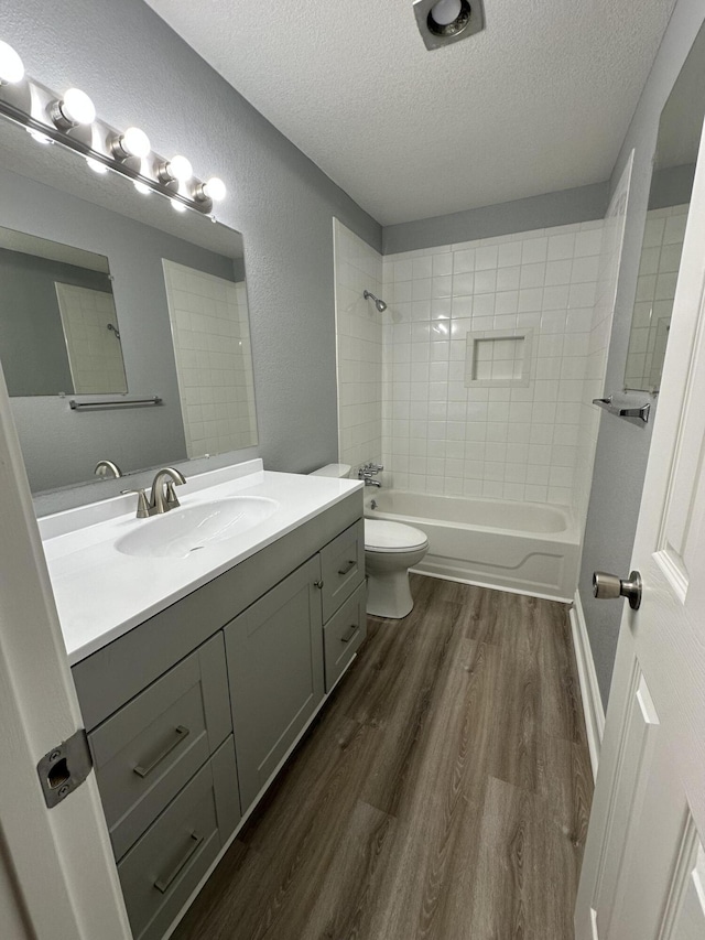 full bathroom featuring hardwood / wood-style flooring, vanity, a textured ceiling, toilet, and tiled shower / bath