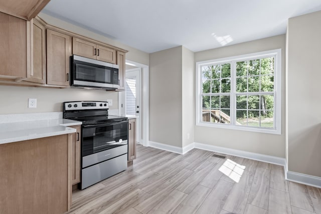 kitchen featuring light stone counters, light brown cabinetry, stainless steel appliances, and light wood-type flooring