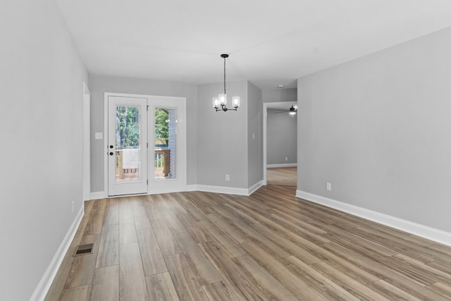 empty room featuring ceiling fan with notable chandelier and light hardwood / wood-style floors