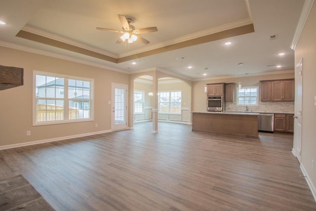 unfurnished living room with ornamental molding, a tray ceiling, ceiling fan, sink, and hardwood / wood-style floors