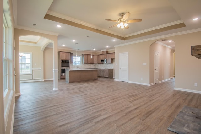 unfurnished living room featuring a tray ceiling, ornamental molding, and light wood-type flooring