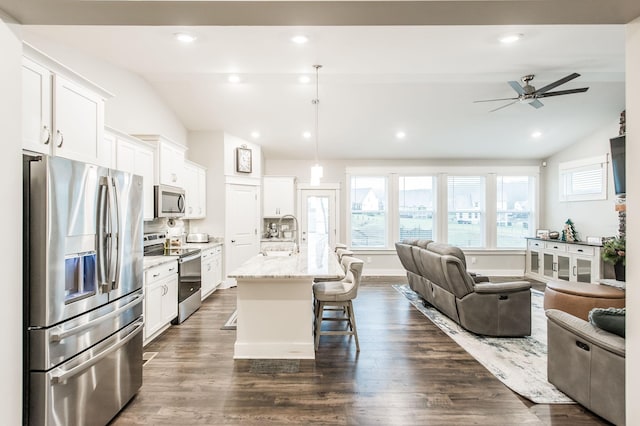 kitchen with white cabinets, appliances with stainless steel finishes, vaulted ceiling, and an island with sink