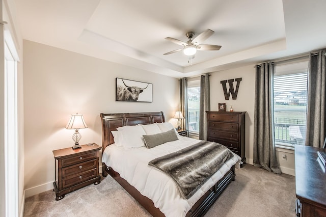 carpeted bedroom featuring a tray ceiling, multiple windows, and ceiling fan