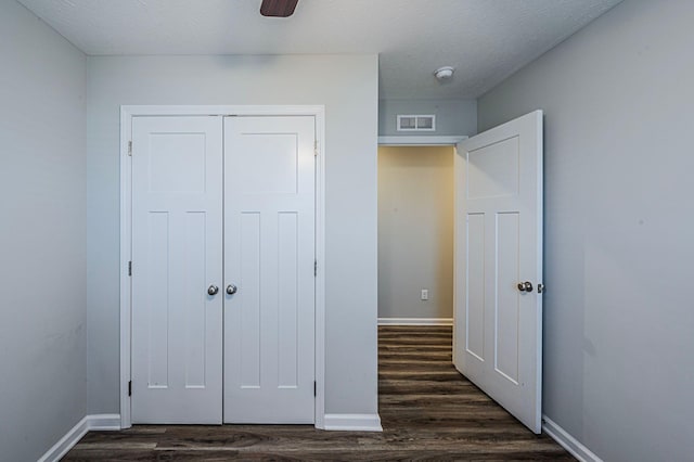 unfurnished bedroom with a textured ceiling, a closet, dark wood-type flooring, and ceiling fan