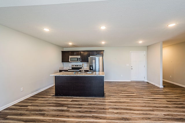 kitchen with appliances with stainless steel finishes, dark hardwood / wood-style flooring, a kitchen island with sink, and sink