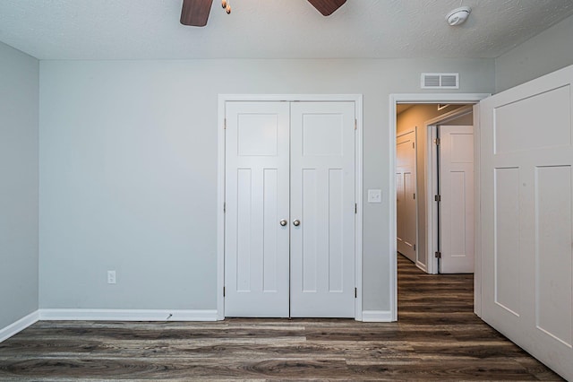 unfurnished bedroom with a textured ceiling, ceiling fan, a closet, and dark hardwood / wood-style floors