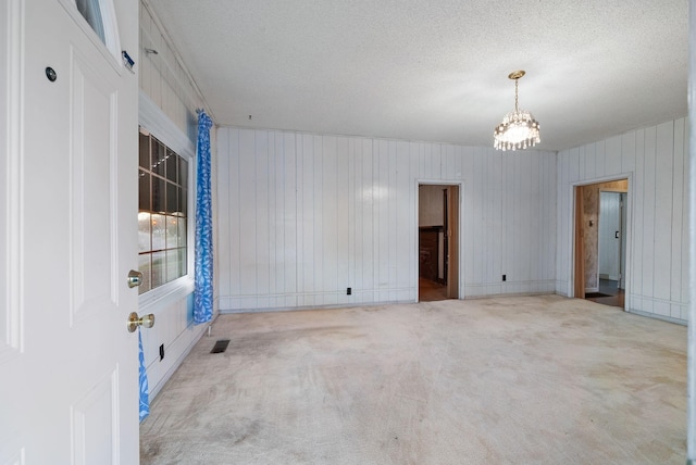 spare room featuring light carpet, wooden walls, and a notable chandelier