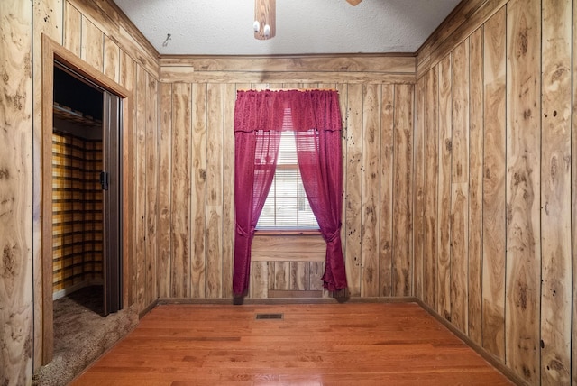 empty room with wood walls, wood-type flooring, and a textured ceiling