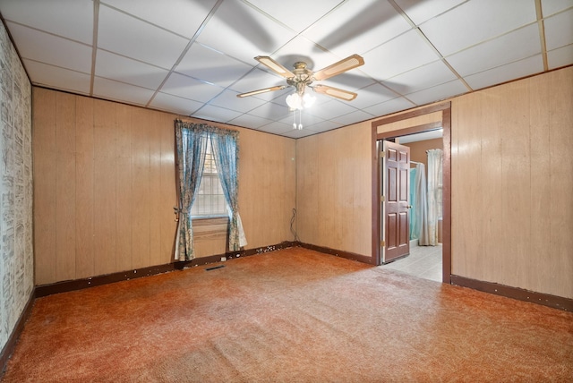 carpeted spare room with a paneled ceiling, ceiling fan, and wooden walls