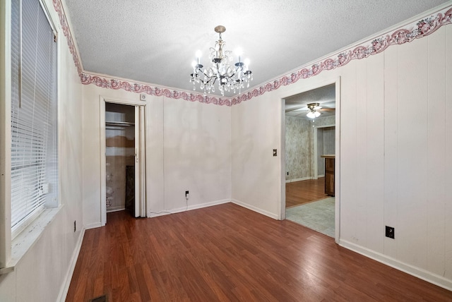 unfurnished room with ceiling fan with notable chandelier, a textured ceiling, crown molding, and dark wood-type flooring