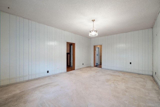 carpeted empty room with a chandelier, a textured ceiling, and wood walls