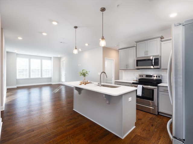 kitchen with sink, dark hardwood / wood-style floors, pendant lighting, a center island with sink, and appliances with stainless steel finishes