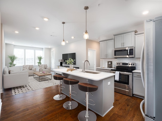 kitchen with sink, hanging light fixtures, an island with sink, dark hardwood / wood-style flooring, and stainless steel appliances