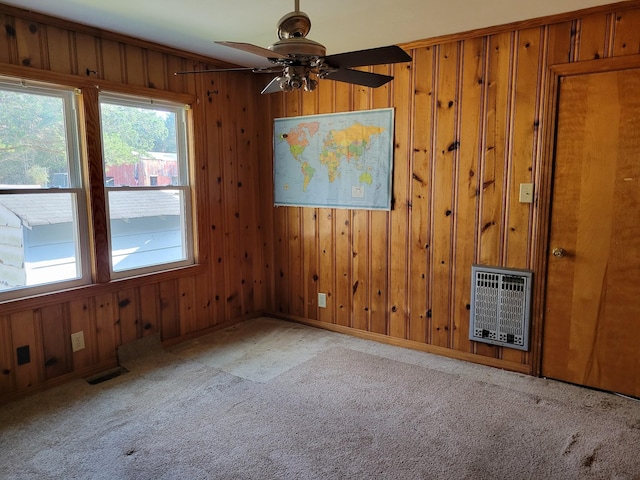 empty room with carpet, heating unit, ceiling fan, and wood walls